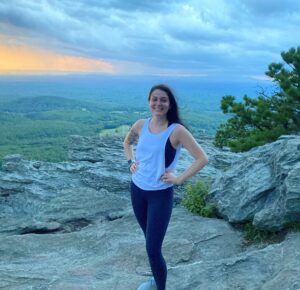 A picture of Stephanie standing on a rocky outcrop, with forests and mountains extending below her to the horizon.